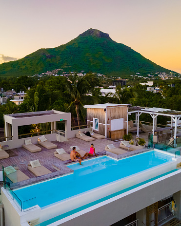 Man and Woman relaxing in a swimming pool watching sunset, a couple on a honeymoon vacation in Mauritius with palm trees and sun beds and on the background mount Tamarin