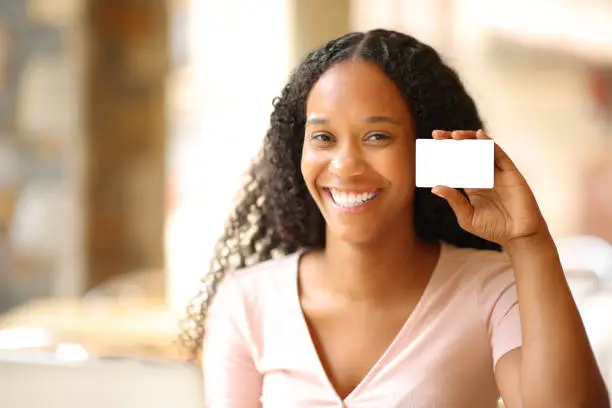 Photo of Black woman showing blank credit card in a bar
