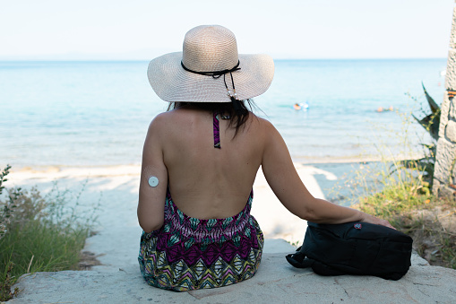 Tourist woman is exploring beautiful small Greek village Afytos on Chalkidiki. She has diabetes and she is wearing small sensor on the back of upper arm for controlling blood sugar.
