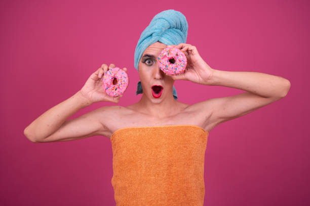 istock Funny drag queen poses in the studio on a pink background and eats donuts. 1593633730