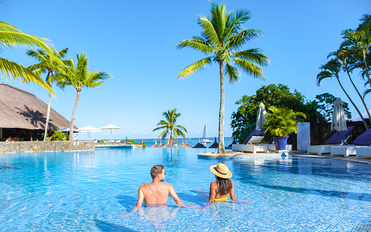Man and Woman relaxing in a swimming pool, a couple on a honeymoon vacation in Mauritius tanning in the pool with palm trees and sun beds