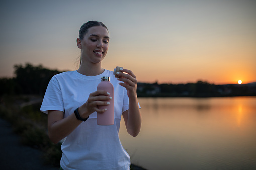 Young beautiful woman drinking water near the river after running