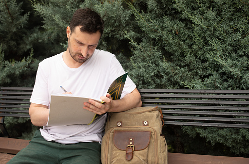 Man writing on a notebook in park. Male student.