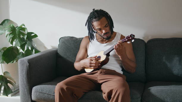 istock Contemporary man playing ukulele closeup. Dreadlocks guy engaging in guitar 1593715153