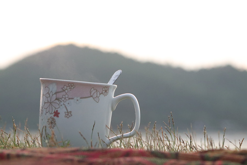 White glass of coffee on grass with blurred island background,Koh yao yai , Thailand