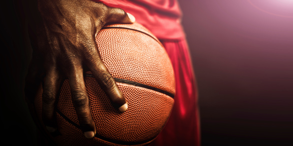 Female basketball player. Beautiful girl holding ball. Side lit half silhouette studio portrait against black background.