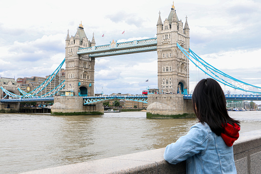 Female Tourist in London, UK, looking at one of the iconic sights of the city, the Tower Bridge over the River Thames