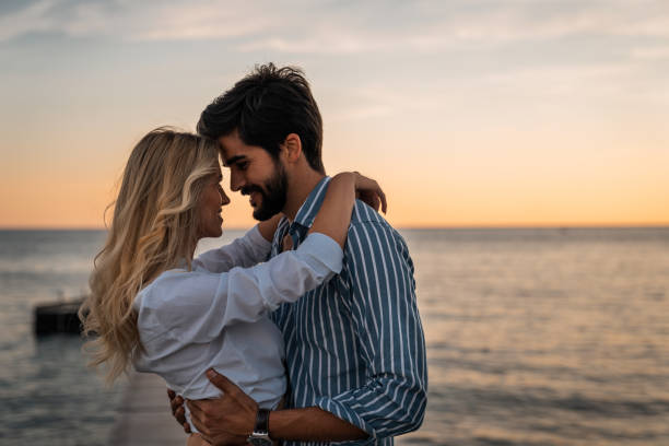Beautiful couple in love standing face to face at sea dock Lovely couple bonding at the beach in summer. Romantic male and female looking each other into eyes during the sunset. Beautiful couple in love standing face to face. falling in love stock pictures, royalty-free photos & images