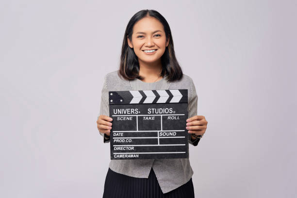 グレイの背景に笑顔の幸せなアジアの若い女性が、古典的な黒いフィルムを作るカチンコを持ちながら、カメラを見ている。人々のライフスタイルファッションコンセプト - slate film slate looking at camera entertainment ストックフォトと画像