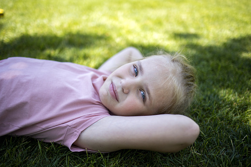Portrait of a cute girl in the park, top view. Happy child playing outdoors in summer. The child is lying on the green grass. Earth Day and the concept of ecology.