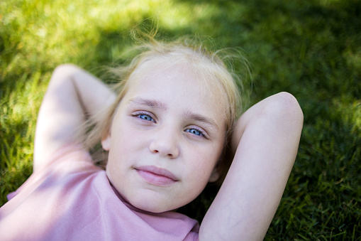 Portrait of a cute girl in the park, top view. Happy child playing outdoors in summer. The child is lying on the green grass. Earth Day and the concept of ecology.