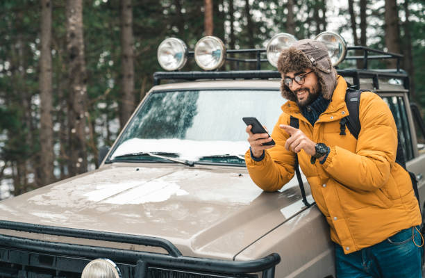 istock Young smiling male using smart phone next to a jeep in the forest 1593820396