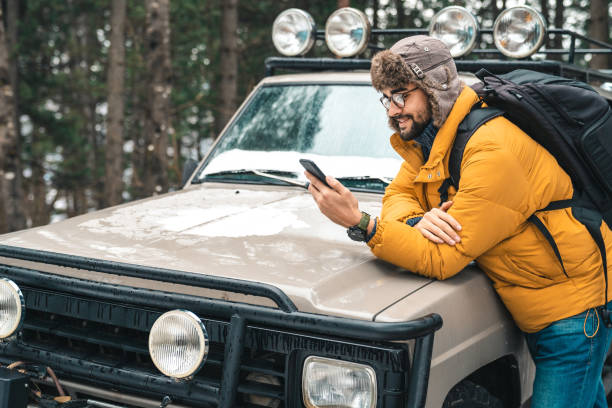 istock Young handsome man with backpack using mobile phone next to a jeep in the forest 1593820415