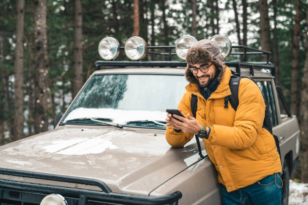 Young happy male using mobile phone next to a jeep in the forest