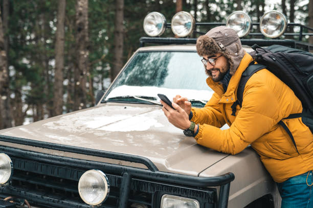 istock Young handsome male explorer using mobile phone next to a jeep in the forest 1593820945