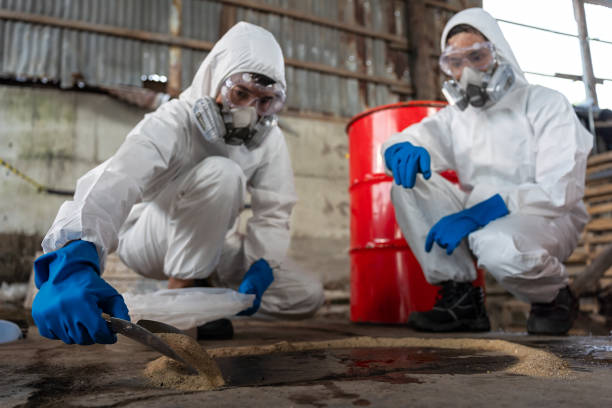 a team of two chemists, wearing ppe suits and gas masks, recover a deadly chemical spill on the factory warehouse floor. correct disposal of chemical spills in industrial plants. - safety sign protective workwear factory imagens e fotografias de stock