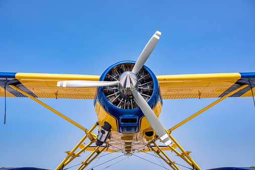 A yellow and blue float plane against a clear blue sky. A portion of the wings can be seen.  The camera is centered on the nose and propeller.