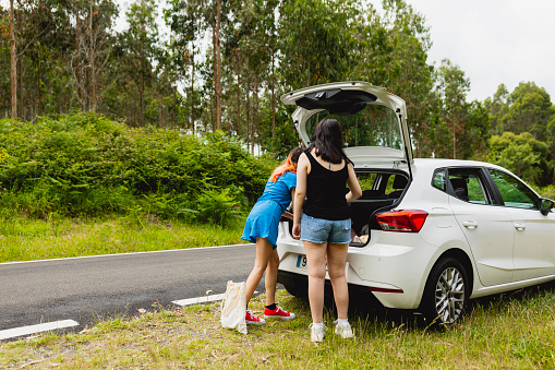 Two young women take their backpacks from the trunk of the car for a walk in nature