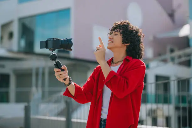Influencer Asian Malay Generation Z young man vlogging in Kuala Lumpur city street sidewalk looking at camera