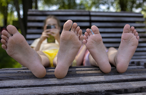 Two girls-sisters of school age relax on a park bench during a walk. View of the feet