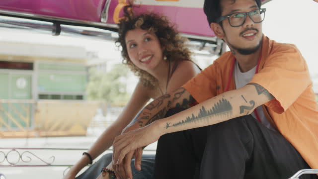 Happy tourist couple sitting in a Tuk-Tuk and traveling around Bangkok city on vacation.