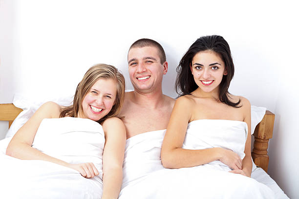 Man with two hot girls being happy for the situation Smiling man in bed between two attractive women- threesome menage trois stock pictures, royalty-free photos & images