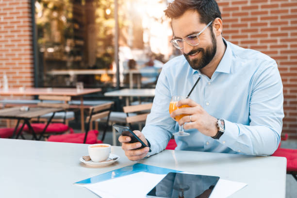 istock Businessman using phone drinking orange juice and reading some texts on his phone 1594037210