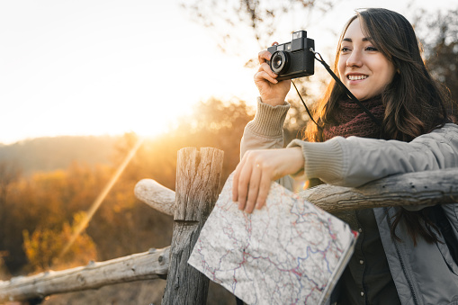 Cheerful female explorer holding a map and taking photos in nature. Close-up photo of young woman spending time in mountains.