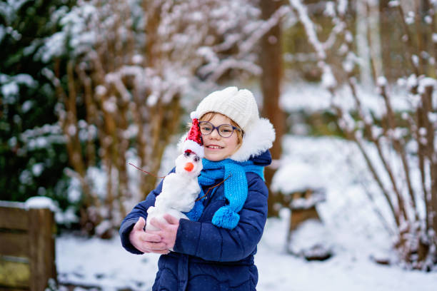 милая маленькая дошкольница в очках делает мини-снеговика. очаровательный здоровый счастливый ребенок играет и веселится со снегом, на све - playground snow winter little girls стоковые фото и изображения