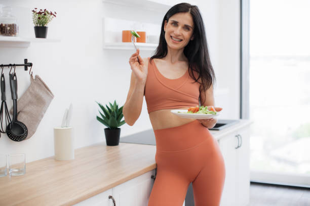 istock Skinny lady leaning on kitchen surface with salad in hands 1594114658