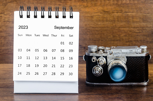 September 2023 Monthly desk calendar for the organizer to plan 2023 year with a vintage camera against a wooden table background.