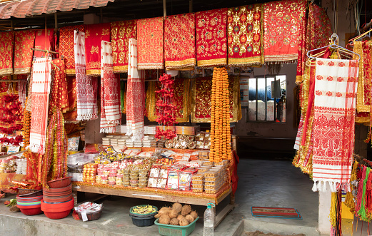 Guwahati, India - 10th April 2023: A market stall selling items such as gamosas, shawls, Indian fabrics, garlands, sweetmeats ,coconuts and diva lamps, on the road leading to the Kamakhya Temple; Guwahati; Assam; India.