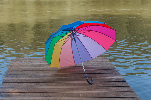 a rainbow-colored umbrella lies open on a bridge by the river