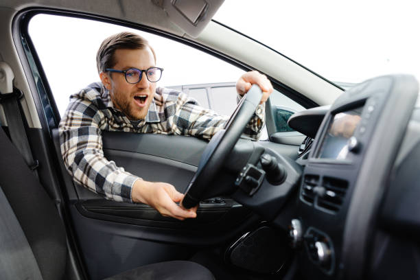 istock Young man looking through window inside new car, checking it before purchase at modern dealership store. Cheerful guy buying or renting automobile at showroom 1594156390