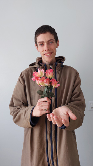 Young man in a beige coat with a bouquet of flowers whit a gray background