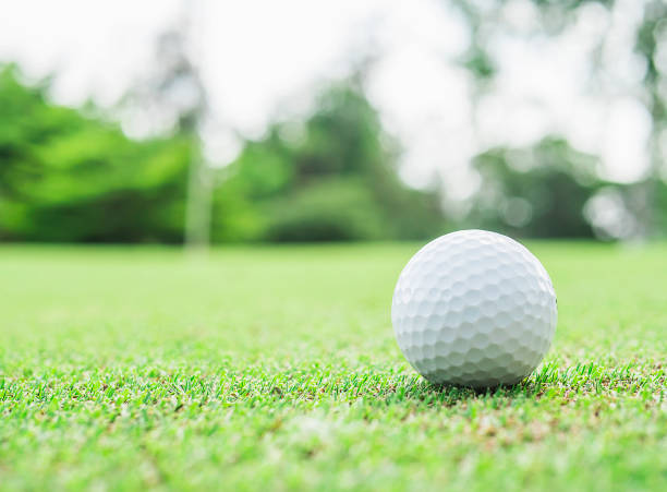 istock Golf ball on green with blurred pin flagstick and green tree background 1594159961