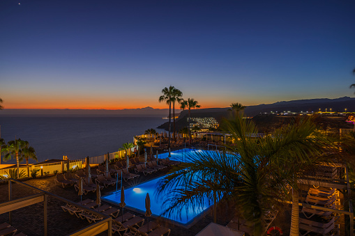 Gran Canaria. Spain. 07.06.2023. Beautiful top view of night illuminated hotel outdoor pool on Atlantic ocean in sunset background. Gran Canaria. Spain.