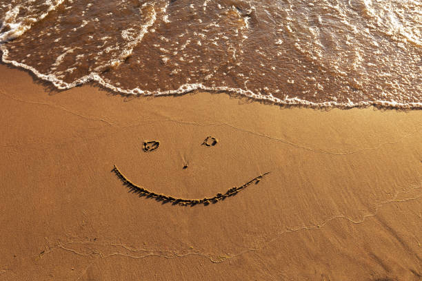 istock emoticon happy smile face painted on jetted beach sand by sea 1594171529