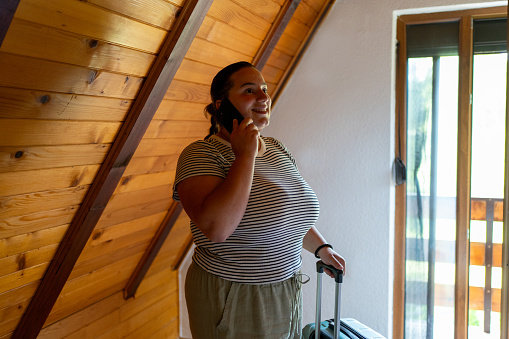 Young beautiful woman talking on a mobile phone while arriving to log cabin for vacation