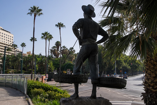 Malaga, Andalusia, Spain - July 29, 2023: Parque de la Marina and sculpture against the light of the Cenachero, work of the artist Jaime Fernández Pimentel, inaugurated in 1968