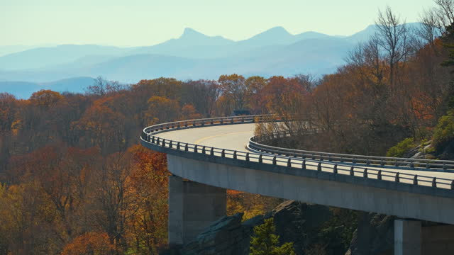 Mountain fall landscape with Linn Cove Viaduct, near Blowing Rock, Blue Ridge Parkway, North Carolina, USA. Driving cars on scenic road between autumnal woods