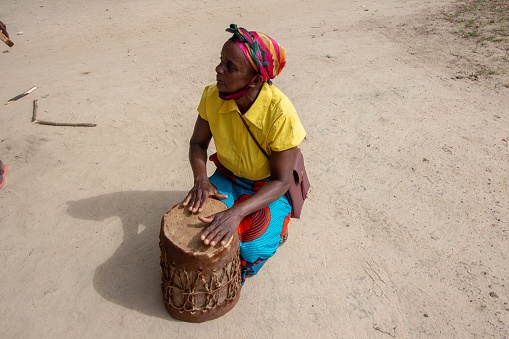 Manica, Mozambique - March 17, 2022: Woman playing drums in the sand, using traditional sarong fabrics