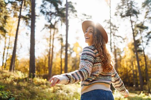 Beautiful young woman in a hat enjoys the autumn weather in a sunny park. Fashion, style concept. The concept of people, lifestyle.