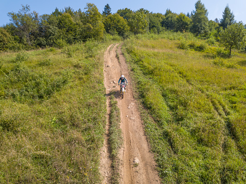 Ukraine, Vizhnitsa - August 25, 2018: Enduro athlete on the forest path on a sunny summer day. Aerial drone view