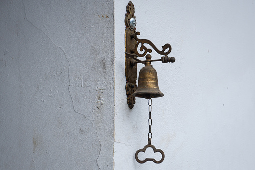 A small brass bell is mounted on the wall of the house to be used as a bell when guests visit.
