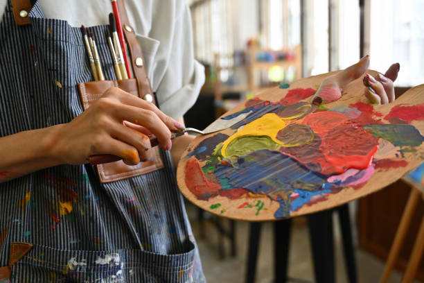 imagen en primer plano de las manos de un joven artista creativo manchadas con acuarelas sosteniendo una espátula mezclando color en una paleta. - fine art painting fotografías e imágenes de stock