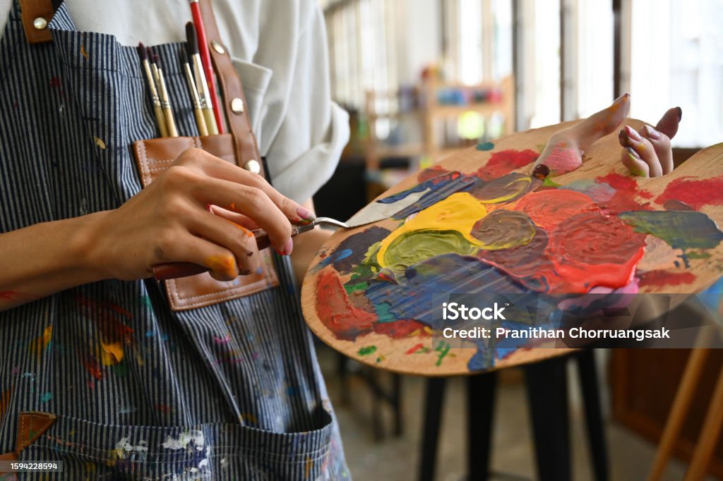 Image en gros plan des mains d’un jeune artiste créatif maculées d’aquarelles tenant une spatule mélangeant des couleurs sur une palette. - Photo de Peindre libre de droits Image en gros plan des mains d’un jeune artiste créatif maculées d’aquarelles tenant une spatule mélangeant des couleurs sur une palette. - Photo de Peindre libre de droits