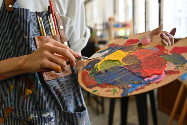 immagine ravvicinata delle mani di un giovane artista creativo imbrattate di acquerelli che reggono una spatola che mescola il colore su una tavolozza. - painting foto e immagini stock