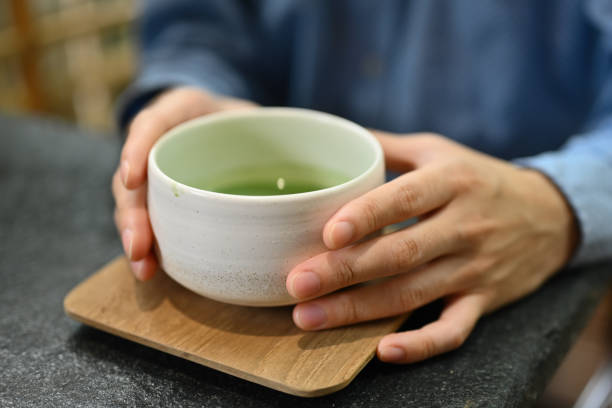 Close up and cropped image of man's hands holding tea cup , Japanese traditional matcha tea, Genmaicha Uji latte in the Japanese tradition ceramic bowl. Close up and cropped image of man's hands holding tea cup , Japanese traditional matcha tea, Genmaicha Uji latte in the Japanese tradition ceramic bowl.. Green Tea for Men's Fitness stock pictures, royalty-free photos & images