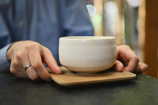 Close up and cropped image of man's hands holding tea cup, Japanese traditional matcha tea.